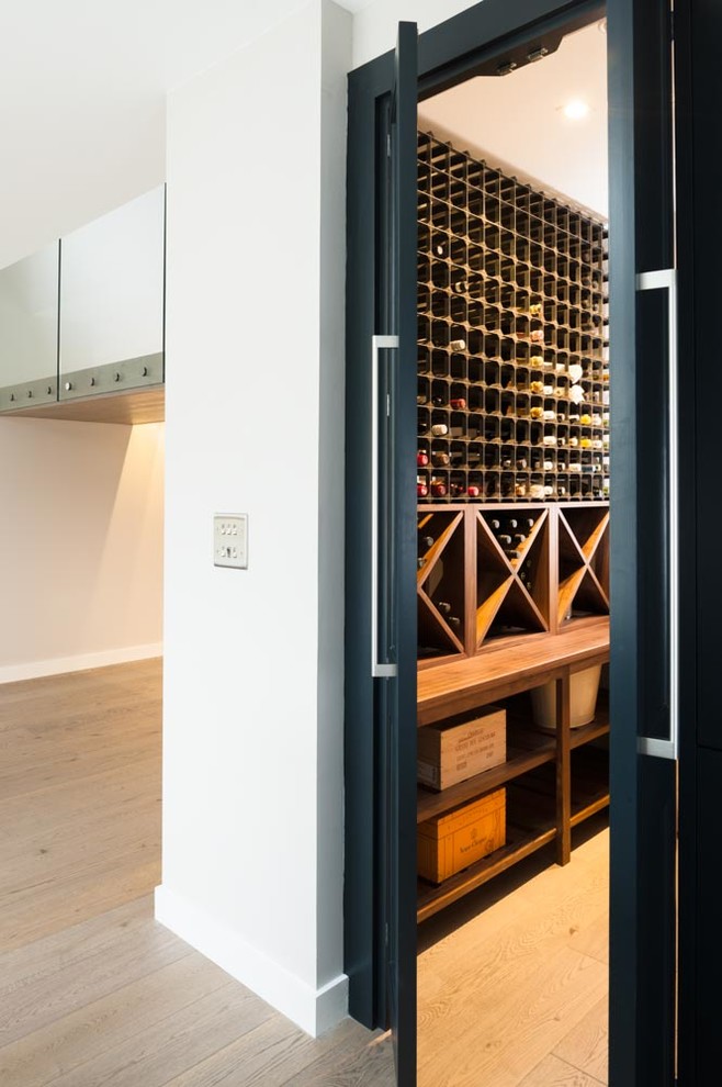 Photo of a large contemporary wine cellar in Kent with light hardwood floors and display racks.