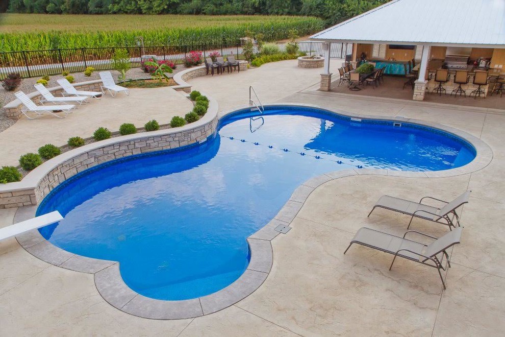 This is an example of a mid-sized transitional backyard custom-shaped lap pool in St Louis with a water feature and concrete pavers.