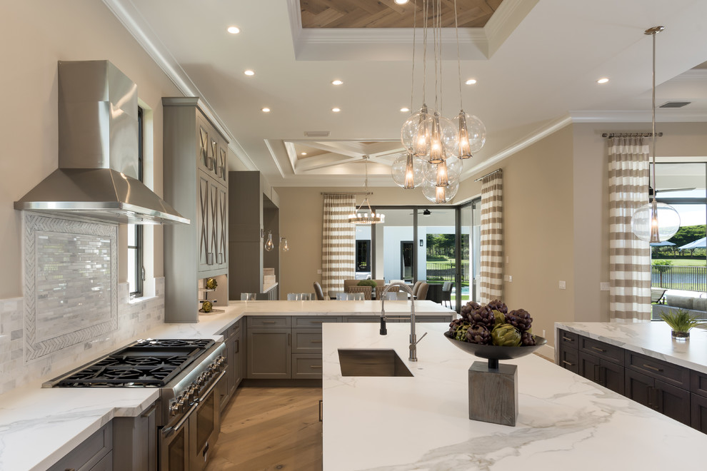 Photo of an expansive transitional l-shaped eat-in kitchen in Miami with a farmhouse sink, flat-panel cabinets, grey cabinets, granite benchtops, white splashback, stone tile splashback, stainless steel appliances, medium hardwood floors and multiple islands.