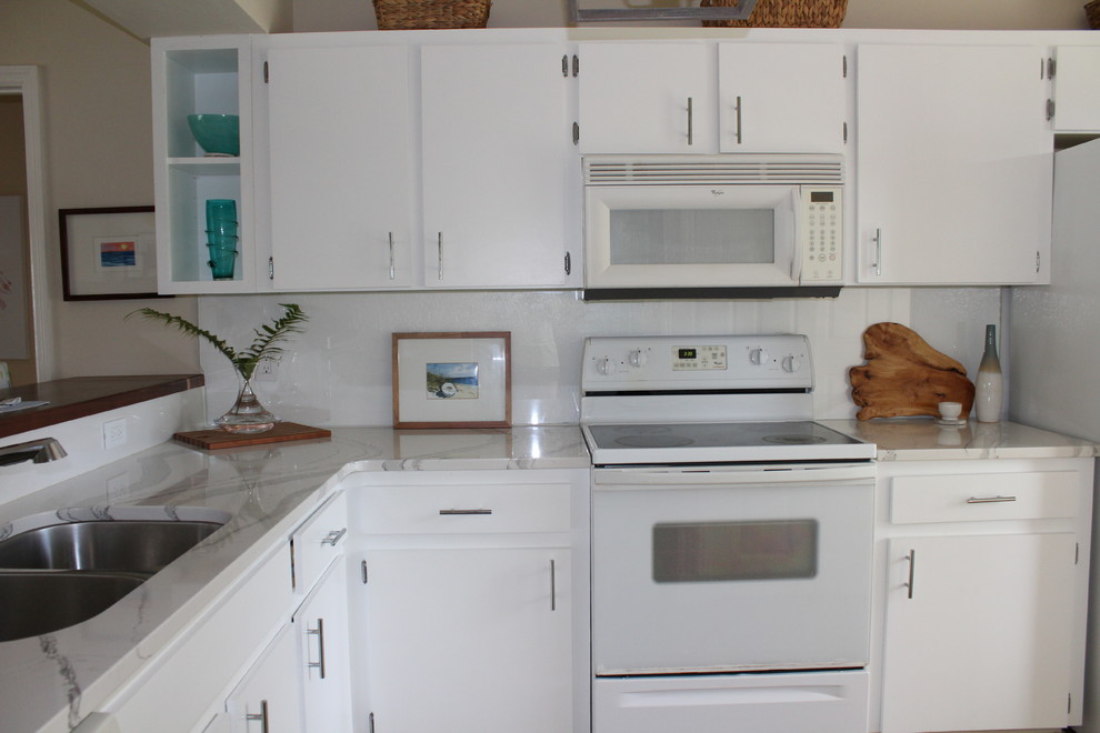 This is an example of a small beach style l-shaped kitchen in Orlando with an undermount sink, flat-panel cabinets, white cabinets, quartz benchtops, white splashback, glass sheet splashback, white appliances, medium hardwood floors and no island.
