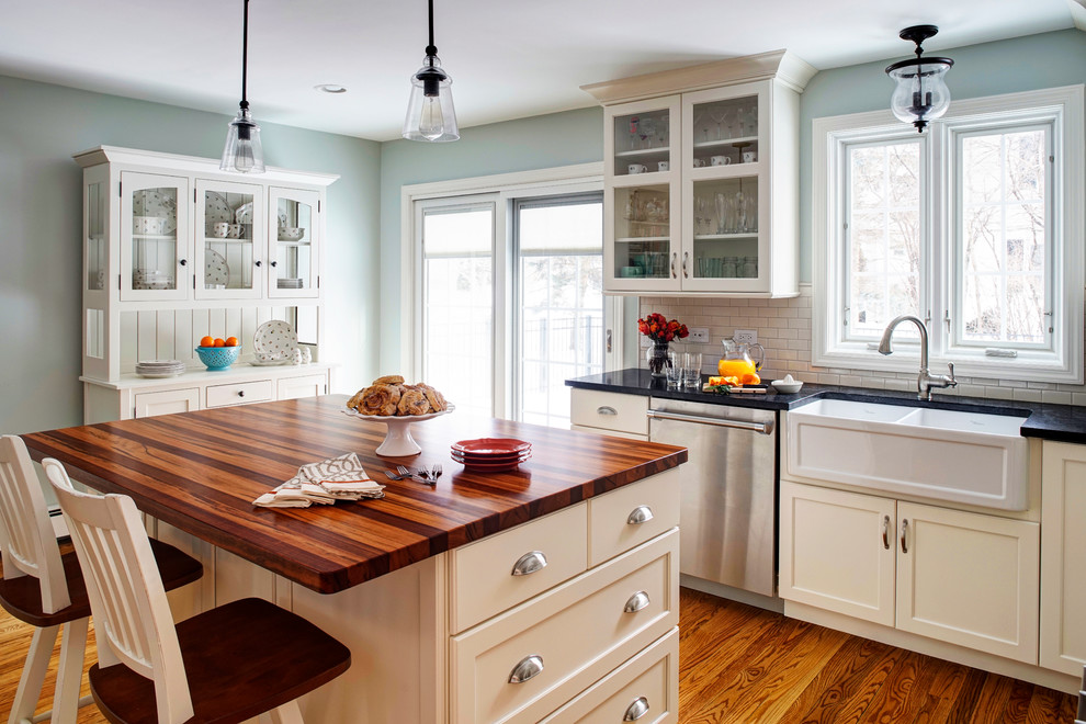 Mid-sized cottage u-shaped medium tone wood floor enclosed kitchen photo in Chicago with a farmhouse sink, shaker cabinets, white cabinets, granite countertops, white backsplash, subway tile backsplash and stainless steel appliances