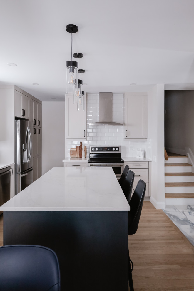 Inspiration for a mid-sized transitional l-shaped medium tone wood floor and brown floor eat-in kitchen remodel in Ottawa with an undermount sink, shaker cabinets, gray cabinets, quartz countertops, white backsplash, subway tile backsplash, stainless steel appliances, an island and white countertops