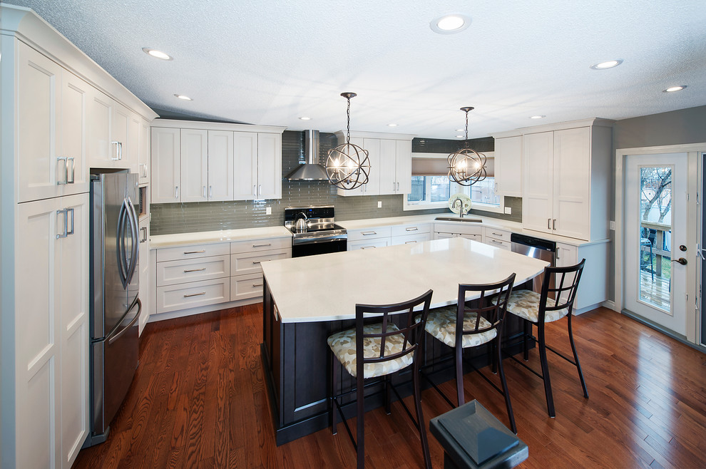 Example of a large transitional l-shaped dark wood floor eat-in kitchen design in Calgary with an undermount sink, recessed-panel cabinets, white cabinets, solid surface countertops, green backsplash, glass tile backsplash, stainless steel appliances and an island