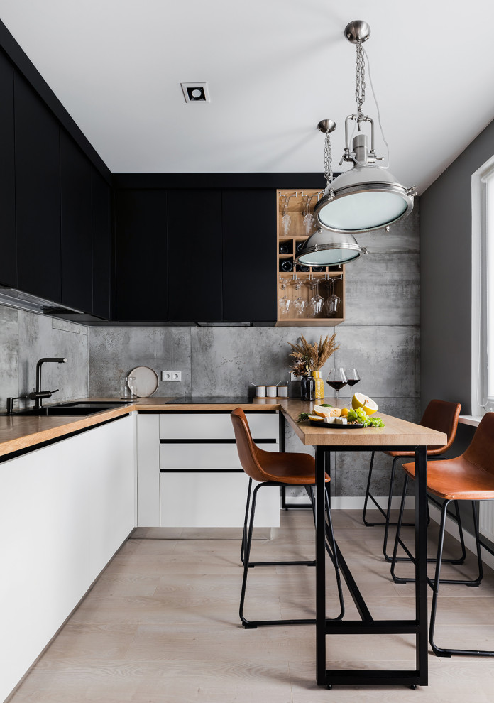 This is an example of a small contemporary l-shaped eat-in kitchen in Saint Petersburg with an undermount sink, flat-panel cabinets, black cabinets, wood benchtops, grey splashback, porcelain splashback, black appliances, laminate floors, no island, beige floor and beige benchtop.