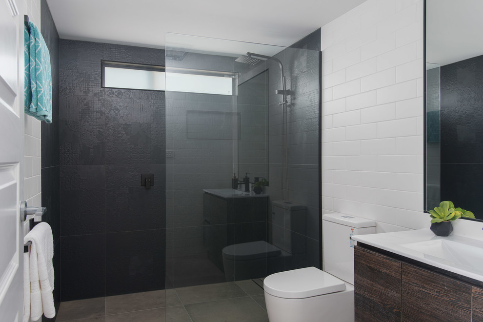 Photo of a mid-sized contemporary master bathroom in Other with recessed-panel cabinets, dark wood cabinets, an open shower, a one-piece toilet, black and white tile, porcelain tile, white walls, ceramic floors, a wall-mount sink, solid surface benchtops, grey floor, an open shower and white benchtops.