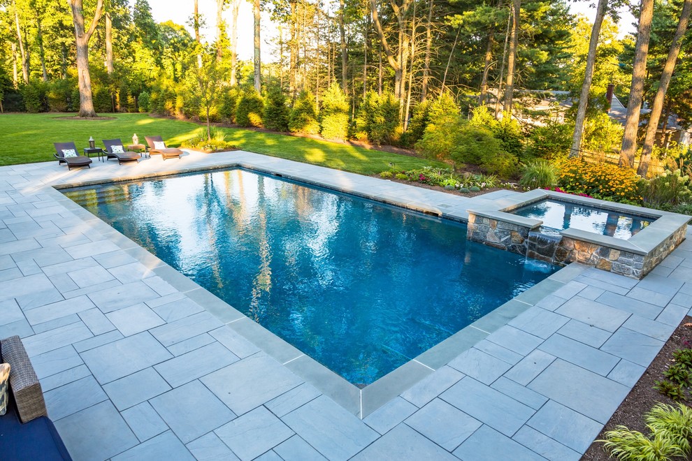 This is an example of a large traditional backyard pool in New York with natural stone pavers.