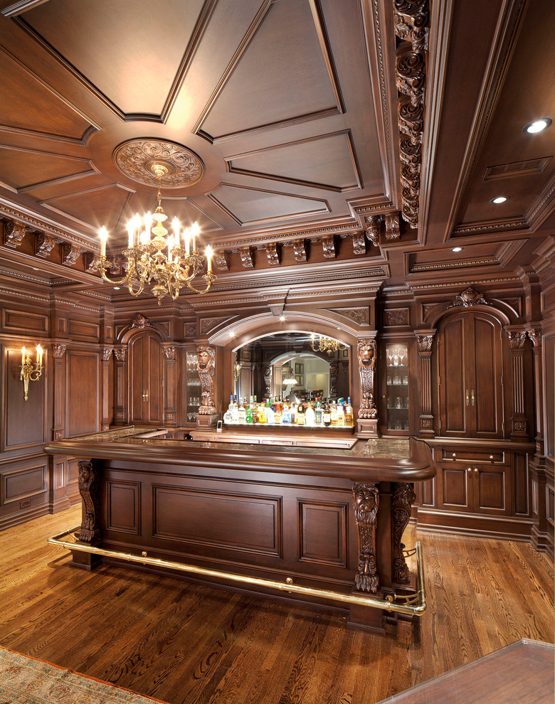 This is an example of a large traditional u-shaped seated home bar in DC Metro with an undermount sink, raised-panel cabinets, brown cabinets, granite benchtops, medium hardwood floors and brown floor.