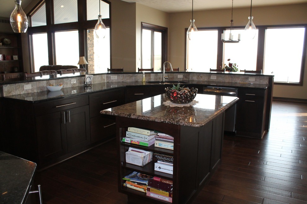 Large transitional single-wall dark wood floor and brown floor open concept kitchen photo with an undermount sink, dark wood cabinets, granite countertops, beige backsplash, stainless steel appliances, beige walls, two islands, shaker cabinets and stone tile backsplash