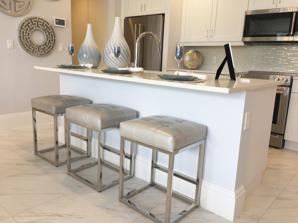 Example of a transitional single-wall white floor kitchen design in Miami with an integrated sink, recessed-panel cabinets, white cabinets, metallic backsplash, glass tile backsplash and an island