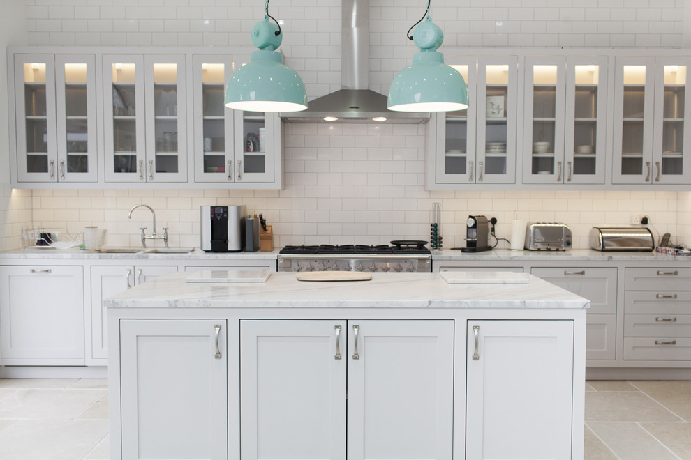 Design ideas for a transitional kitchen in Surrey with a double-bowl sink, glass-front cabinets, white cabinets, white splashback, subway tile splashback, stainless steel appliances and with island.