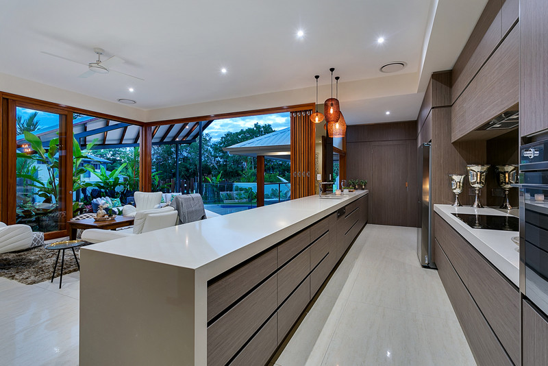 Large tropical galley eat-in kitchen in Cairns with an undermount sink, quartz benchtops, metallic splashback, glass sheet splashback, stainless steel appliances, porcelain floors and with island.