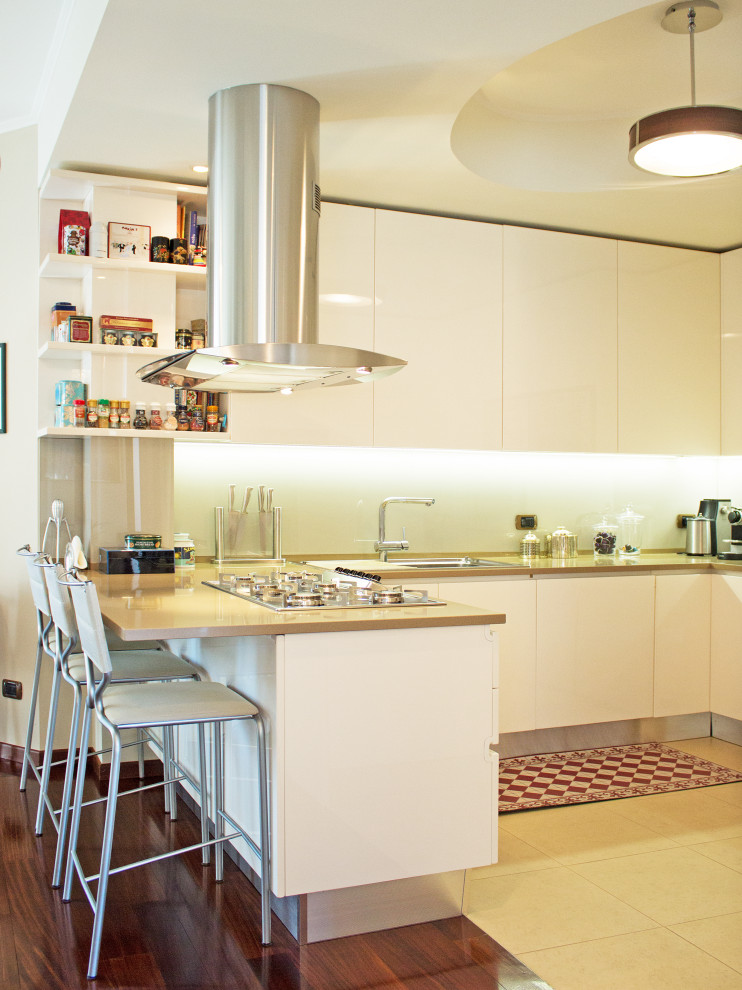 This is an example of a large modern l-shaped open plan kitchen in Milan with a drop-in sink, flat-panel cabinets, white cabinets, limestone benchtops, white splashback, panelled appliances, porcelain floors, with island, beige floor and beige benchtop.