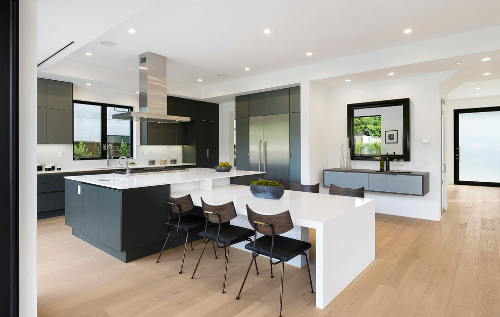 Contemporary l-shaped kitchen in Los Angeles with a drop-in sink, flat-panel cabinets, dark wood cabinets, quartz benchtops, glass sheet splashback, stainless steel appliances, with island and white benchtop.