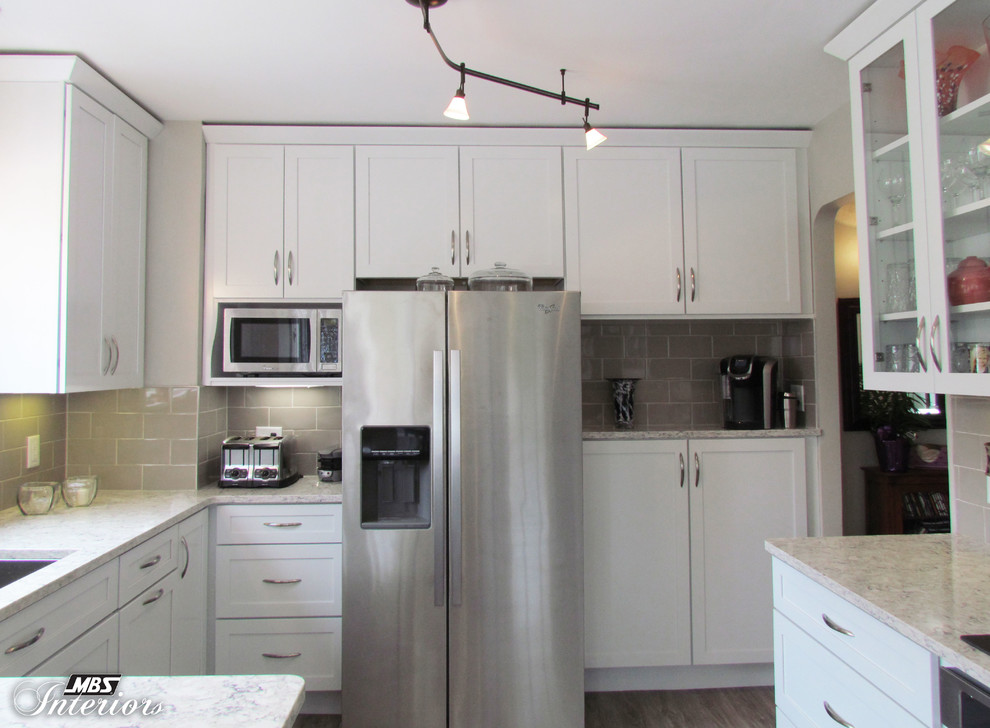 This is an example of a mid-sized contemporary u-shaped eat-in kitchen in Detroit with an undermount sink, shaker cabinets, white cabinets, quartz benchtops, beige splashback, glass tile splashback, stainless steel appliances, no island, medium hardwood floors and grey floor.