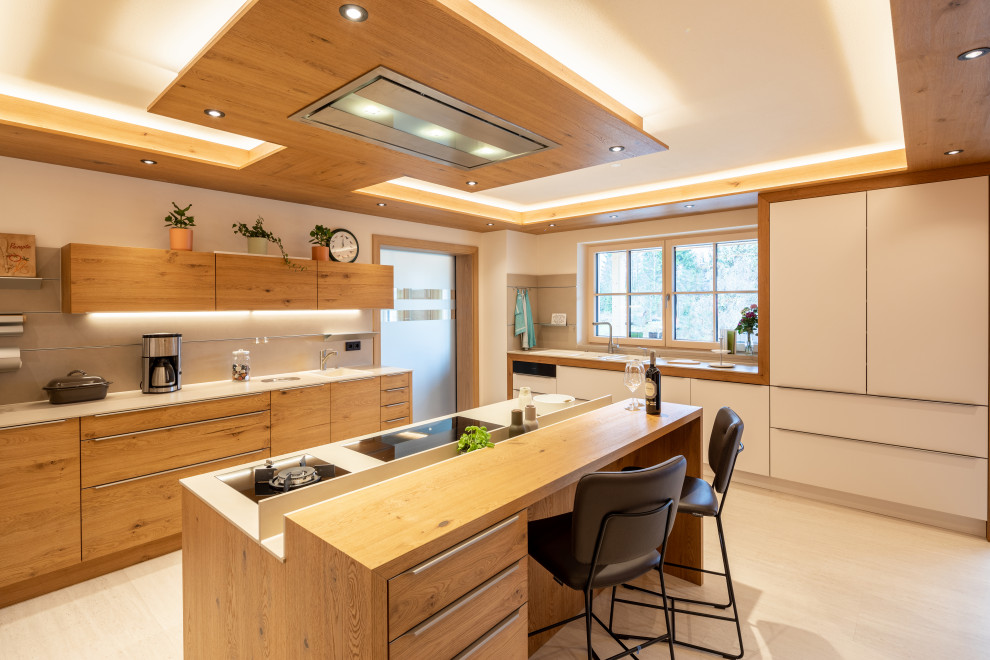 Photo of a large asian l-shaped kitchen with flat-panel cabinets, light wood cabinets, grey splashback, stainless steel appliances, with island, beige floor and white benchtop.