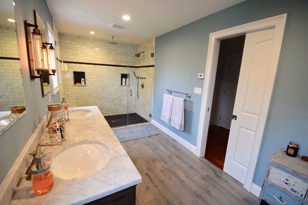 Large transitional master gray tile and marble tile porcelain tile and brown floor doorless shower photo with recessed-panel cabinets, dark wood cabinets, blue walls, an undermount sink, marble countertops, a hinged shower door, gray countertops and a one-piece toilet