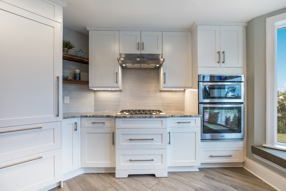 Inspiration for a beach style kitchen in Jacksonville with an undermount sink, shaker cabinets, white cabinets, granite benchtops, white splashback, limestone splashback, stainless steel appliances, ceramic floors, with island, grey floor and brown benchtop.