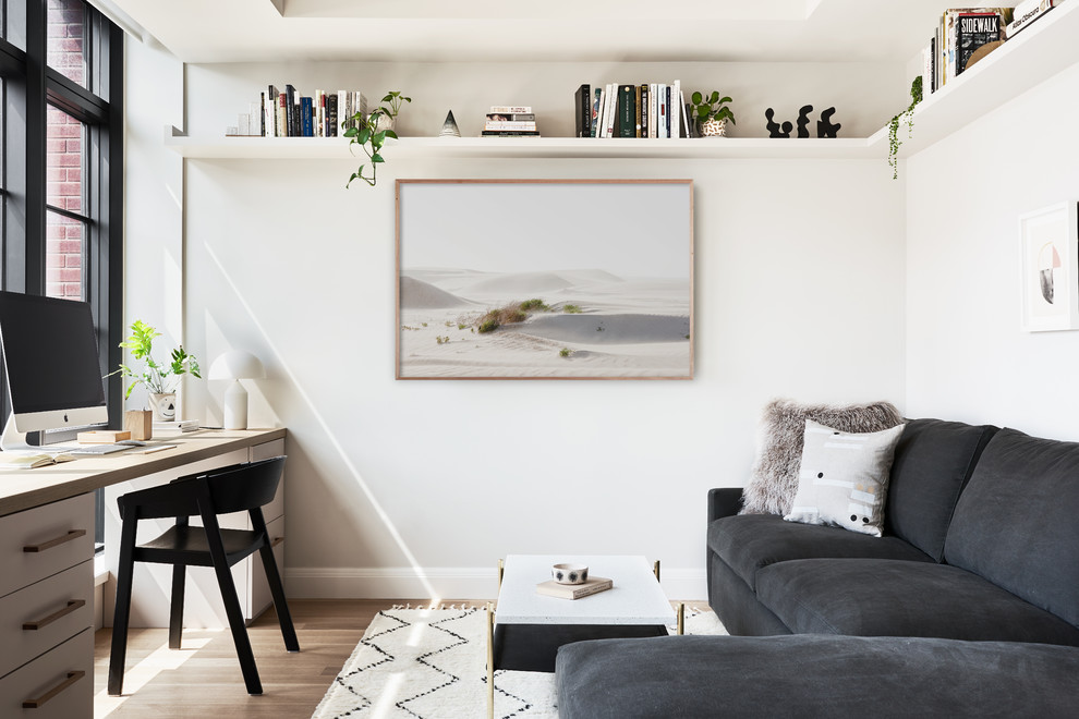 Photo of a scandinavian home office in New York with a library, white walls, light hardwood floors and no fireplace.