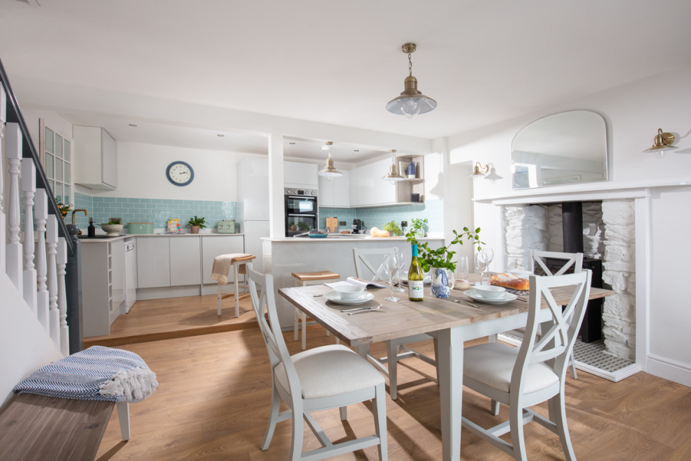 Mittelgroße Klassische Wohnküche mit weißer Wandfarbe, braunem Holzboden, Kaminofen, Kaminumrandung aus gestapelten Steinen und braunem Boden in Cornwall