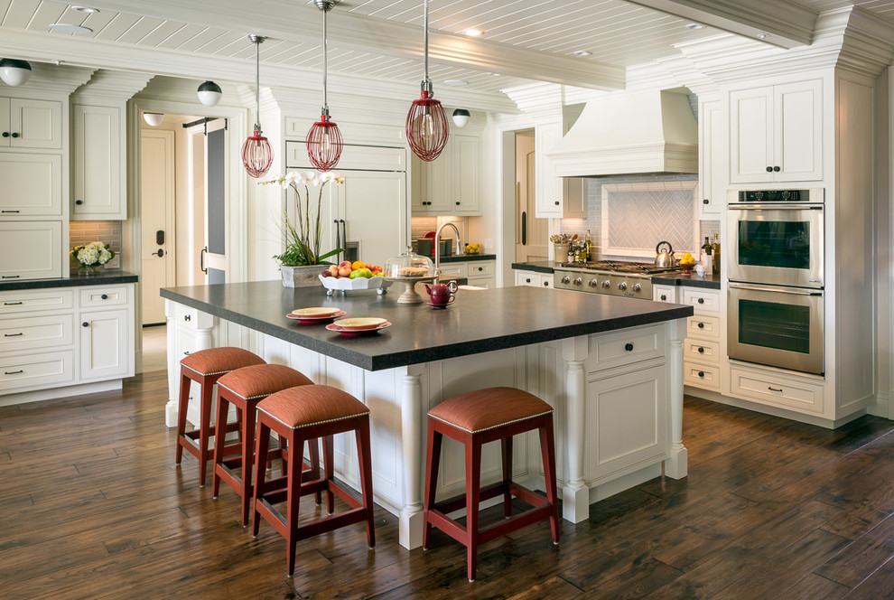 Photo of a large traditional l-shaped kitchen in San Francisco with a farmhouse sink, beaded inset cabinets, white cabinets, grey splashback, ceramic splashback, dark hardwood floors, with island and stainless steel appliances.