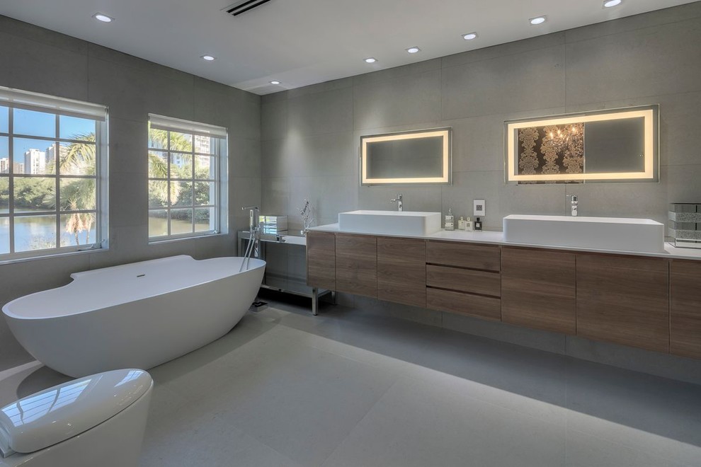 Inspiration for an expansive modern master bathroom in Miami with a trough sink, flat-panel cabinets, a freestanding tub, gray tile, grey walls and dark wood cabinets.