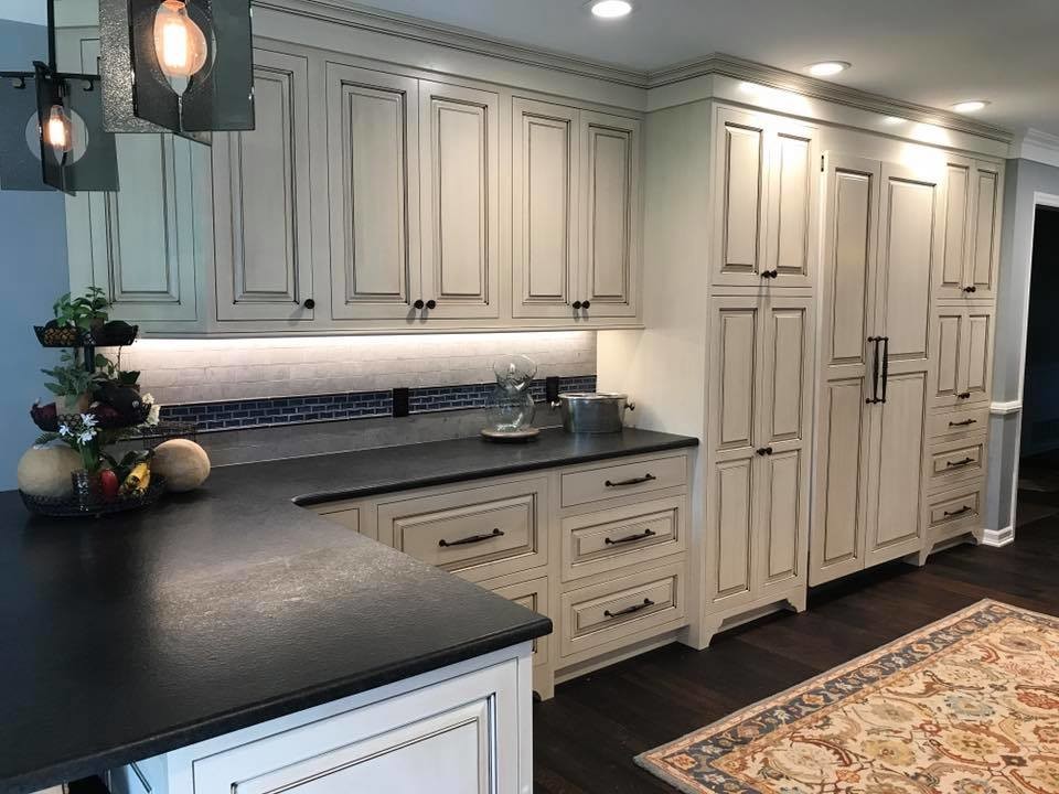 This is an example of a mid-sized country l-shaped eat-in kitchen in Other with a farmhouse sink, distressed cabinets, stainless steel appliances, raised-panel cabinets, soapstone benchtops, grey splashback, ceramic splashback, dark hardwood floors, with island and brown floor.