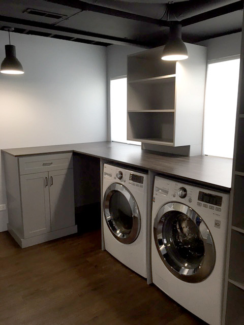 Photo of a large traditional utility room in Chicago with grey cabinets, white walls, dark hardwood floors and a side-by-side washer and dryer.
