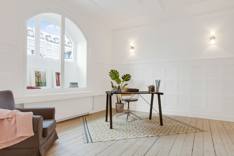 This is an example of a large transitional home office in Copenhagen with white walls, light hardwood floors, no fireplace and a freestanding desk.