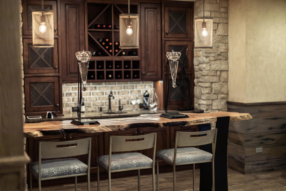 Photo of a mid-sized transitional single-wall seated home bar in Chicago with raised-panel cabinets, medium wood cabinets, beige splashback, stone tile splashback, porcelain floors and brown floor.