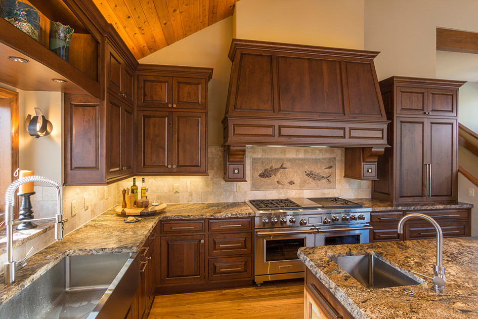 Mid-sized mountain style l-shaped light wood floor eat-in kitchen photo in Denver with a farmhouse sink, raised-panel cabinets, dark wood cabinets, granite countertops, beige backsplash, porcelain backsplash, stainless steel appliances and an island