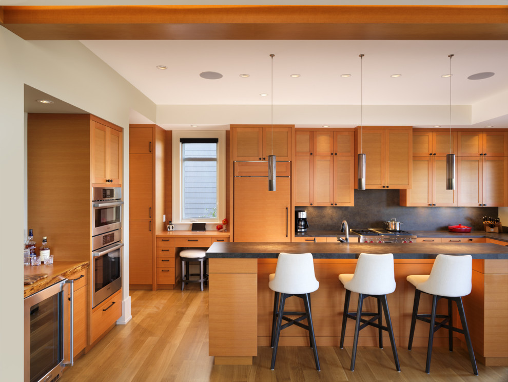 Example of a large transitional l-shaped medium tone wood floor and brown floor eat-in kitchen design with an undermount sink, shaker cabinets, medium tone wood cabinets, solid surface countertops, black backsplash, stone slab backsplash, paneled appliances, an island and black countertops
