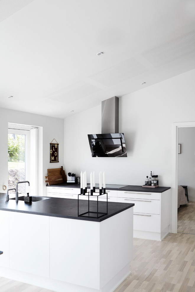 Photo of a mid-sized scandinavian galley open plan kitchen in Wiltshire with a double-bowl sink, flat-panel cabinets, quartzite benchtops, light hardwood floors and a peninsula.