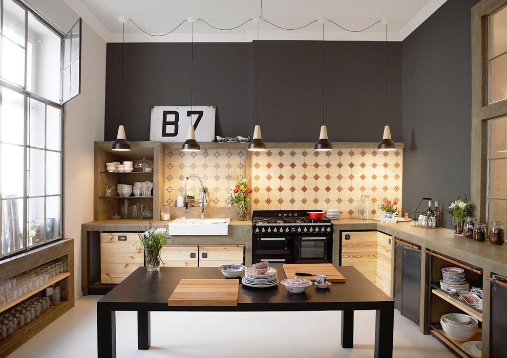 Photo of an industrial l-shaped kitchen in Hamburg with a farmhouse sink, flat-panel cabinets, multi-coloured splashback, black appliances, with island and grey floor.