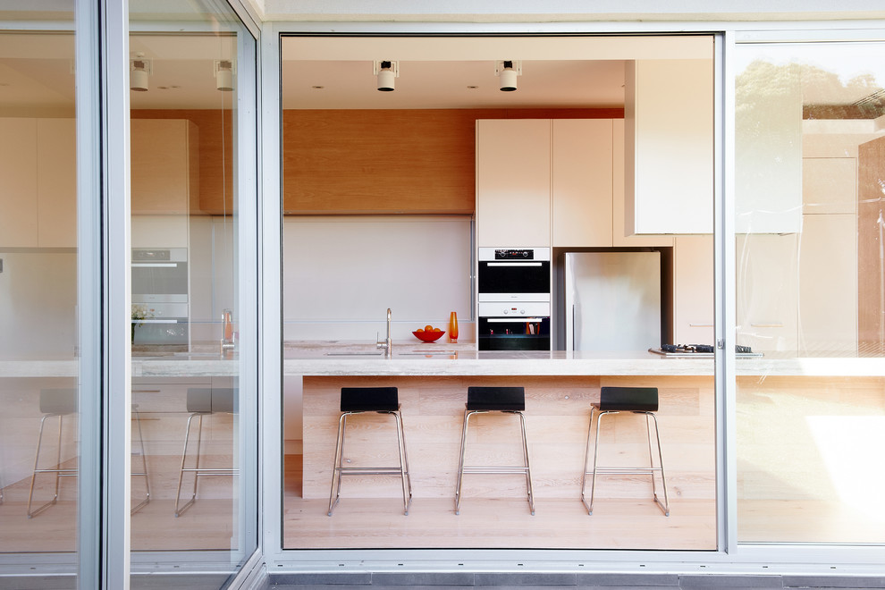 Photo of a large contemporary galley eat-in kitchen in Melbourne with a double-bowl sink, white cabinets, light hardwood floors and with island.