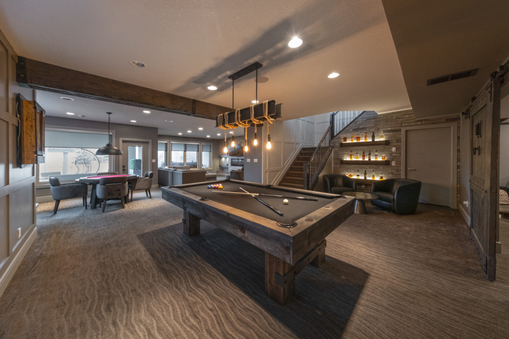 This is an example of a large contemporary walk-out basement in Edmonton with a game room, grey walls, carpet, a standard fireplace, a brick fireplace surround, brown floor, exposed beam and panelled walls.