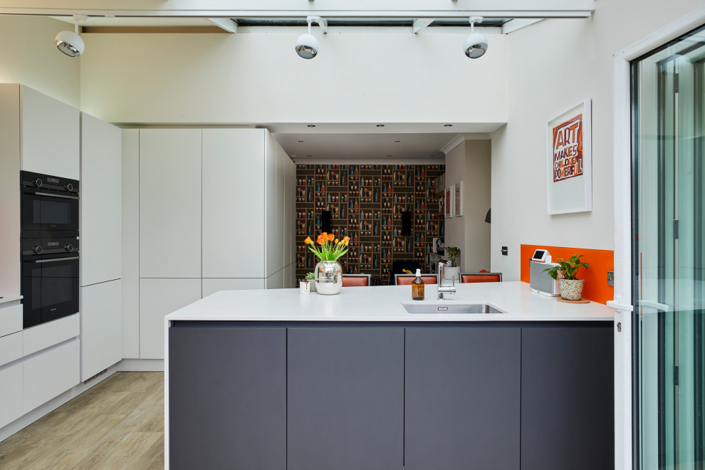 ロンドンにある中くらいなコンテンポラリースタイルのおしゃれなキッチン (アンダーカウンターシンク、フラットパネル扉のキャビネット、白いキャビネット、クオーツストーンカウンター、オレンジのキッチンパネル、ガラス板のキッチンパネル、シルバーの調理設備、淡色無垢フローリング、白いキッチンカウンター) の写真