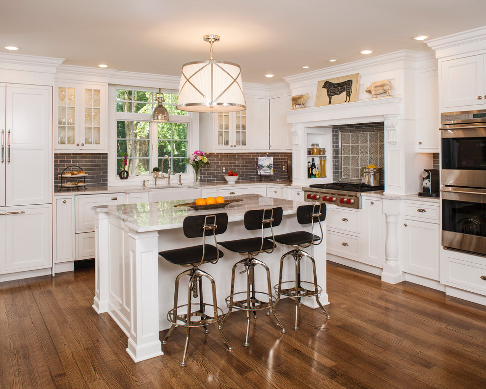 This is an example of a mid-sized country l-shaped kitchen in New York with a farmhouse sink, shaker cabinets, white cabinets, granite benchtops, brown splashback, stainless steel appliances, medium hardwood floors, with island and subway tile splashback.