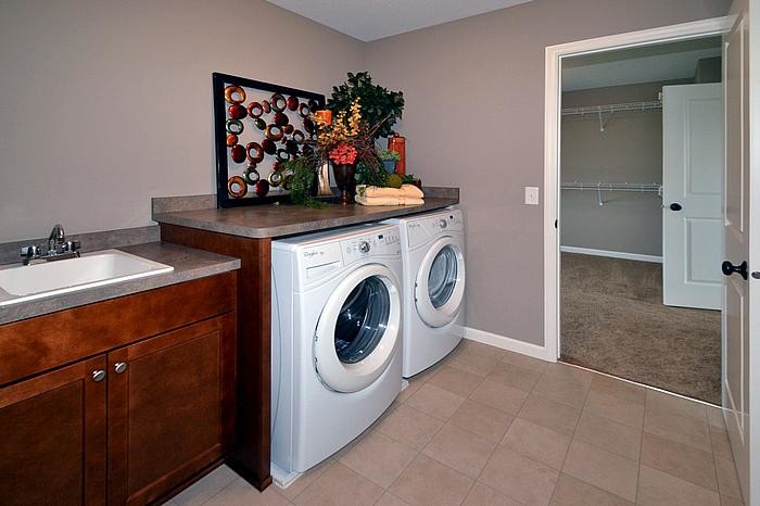 Transitional single-wall dedicated laundry room in Minneapolis with a drop-in sink, shaker cabinets, medium wood cabinets, laminate benchtops, beige walls, vinyl floors and a side-by-side washer and dryer.