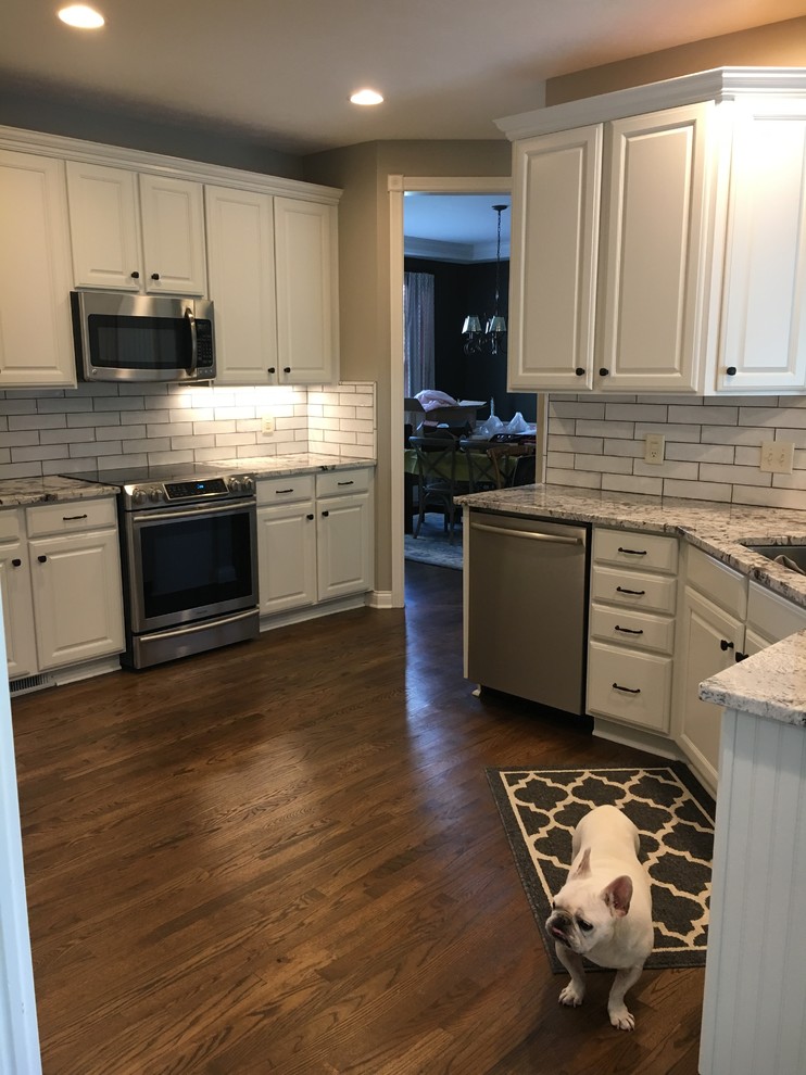 Inspiration for a mid-sized transitional u-shaped medium tone wood floor and brown floor kitchen pantry remodel in Indianapolis with an undermount sink, raised-panel cabinets, white cabinets, granite countertops, white backsplash, ceramic backsplash, stainless steel appliances, no island and white countertops
