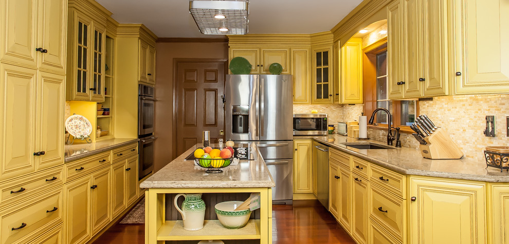 Inspiration for a mid-sized country l-shaped separate kitchen in Baltimore with an undermount sink, beaded inset cabinets, yellow cabinets, quartz benchtops, beige splashback, stone tile splashback, stainless steel appliances, medium hardwood floors, with island and brown floor.