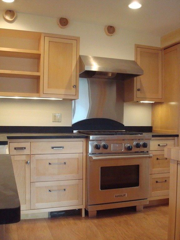 Example of a mid-sized l-shaped medium tone wood floor eat-in kitchen design with medium tone wood cabinets, solid surface countertops, stainless steel appliances and an island
