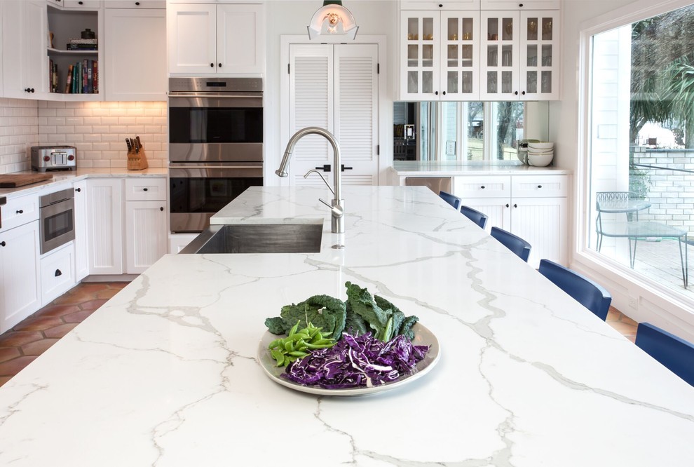 Inspiration for a large transitional l-shaped eat-in kitchen in Charlotte with a farmhouse sink, shaker cabinets, white cabinets, quartz benchtops, white splashback, subway tile splashback, panelled appliances, terra-cotta floors, with island and orange floor.