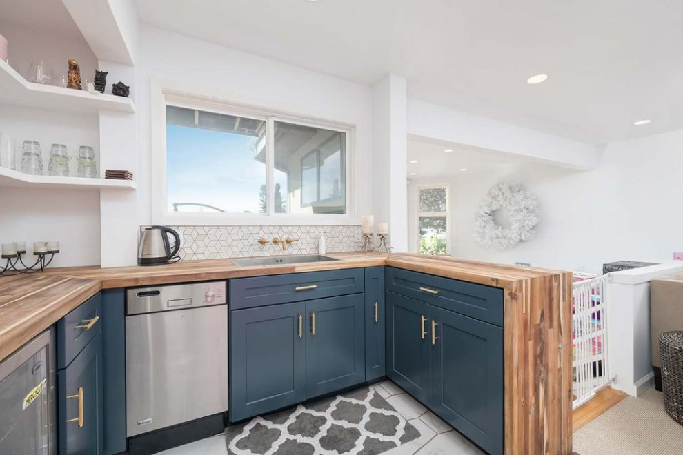 Small transitional u-shaped kitchen in San Francisco with a drop-in sink, shaker cabinets, blue cabinets, wood benchtops, white splashback, porcelain splashback, stainless steel appliances, marble floors, a peninsula, grey floor and brown benchtop.