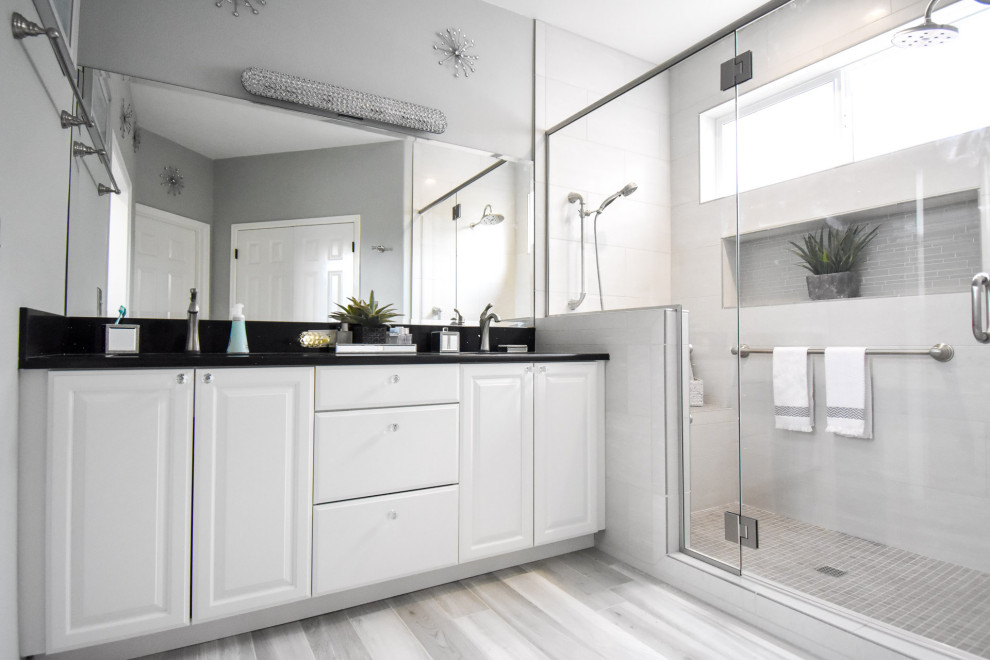 This is an example of a mid-sized transitional master bathroom in Portland with raised-panel cabinets, white cabinets, an alcove shower, a two-piece toilet, gray tile, ceramic tile, grey walls, ceramic floors, an undermount sink, engineered quartz benchtops, grey floor, a hinged shower door, black benchtops, a shower seat, a double vanity and a built-in vanity.