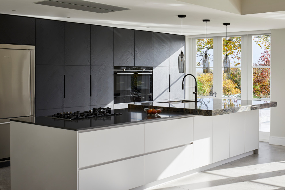 Design ideas for an expansive contemporary galley eat-in kitchen in Kent with flat-panel cabinets, stone slab splashback, stainless steel appliances, porcelain floors, with island, grey floor, an undermount sink, black cabinets and grey benchtop.
