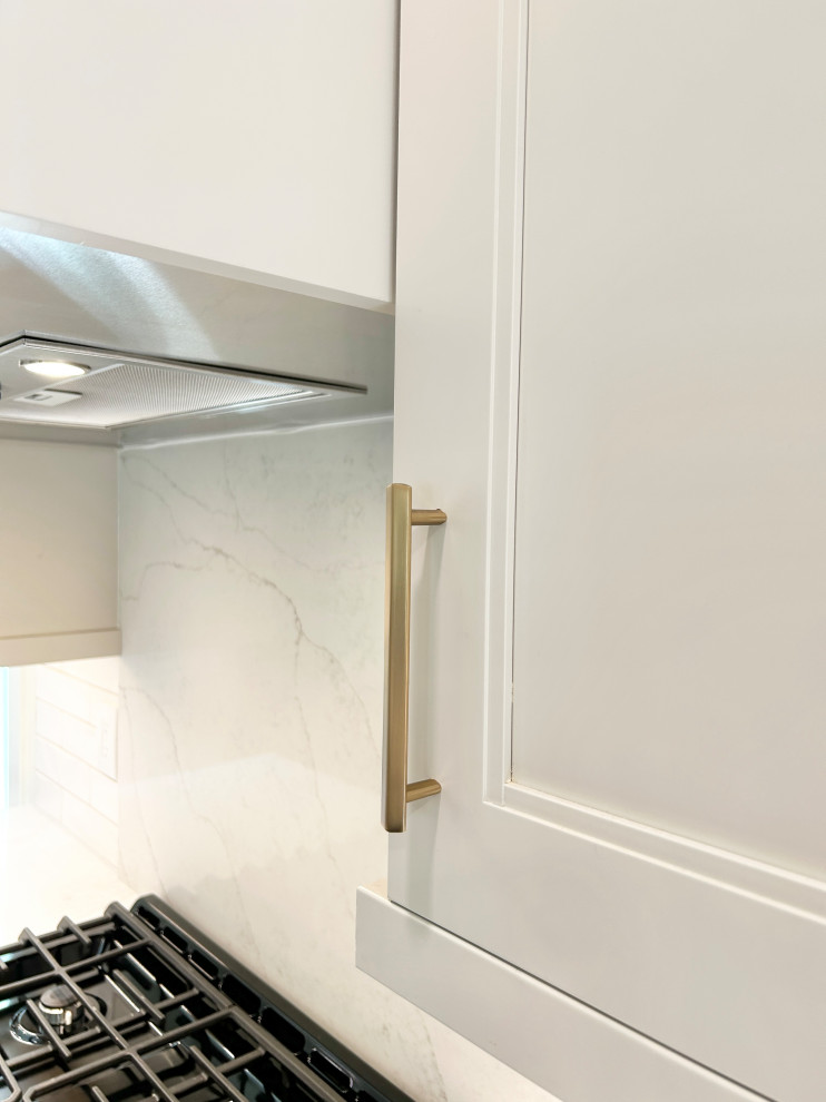 Example of a large transitional u-shaped light wood floor open concept kitchen design with an undermount sink, flat-panel cabinets, white cabinets, quartz countertops, white backsplash, ceramic backsplash, black appliances, an island and white countertops
