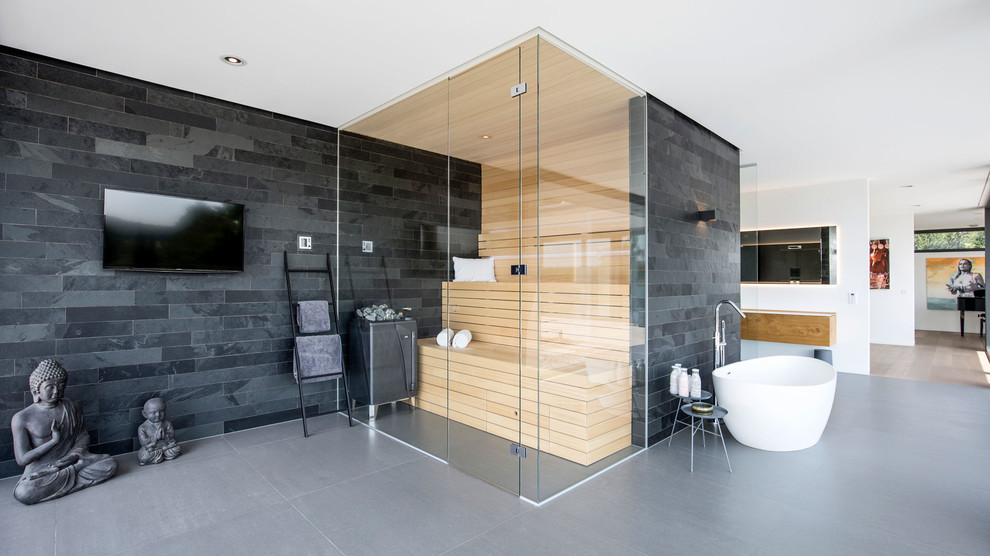 This is an example of an expansive asian bathroom in Dortmund with glass-front cabinets, beige cabinets, a freestanding tub, a curbless shower, a wall-mount toilet, gray tile, stone tile, green walls, ceramic floors, with a sauna, a console sink, grey floor and an open shower.