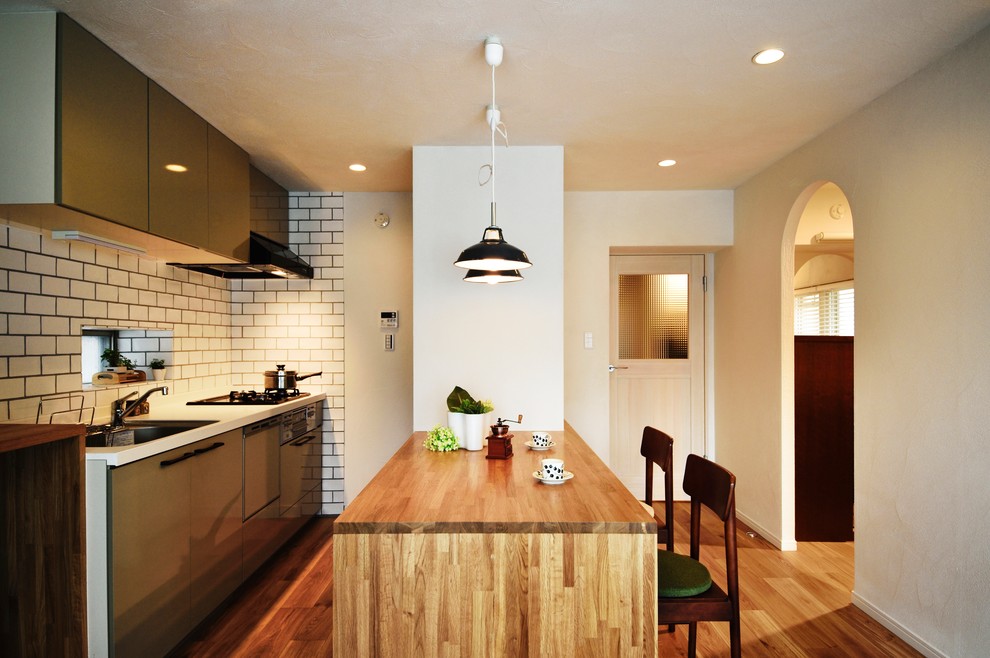 Photo of an asian single-wall kitchen in Other with a single-bowl sink, flat-panel cabinets, grey cabinets, white splashback, subway tile splashback, medium hardwood floors, a peninsula, brown floor and brown benchtop.