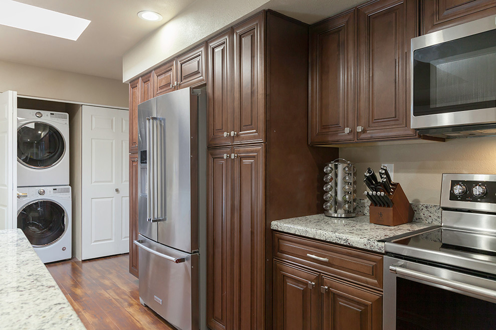 Example of a mid-sized transitional l-shaped laminate floor and brown floor enclosed kitchen design in Phoenix with an undermount sink, shaker cabinets, medium tone wood cabinets, granite countertops, multicolored backsplash, stone slab backsplash, stainless steel appliances and an island