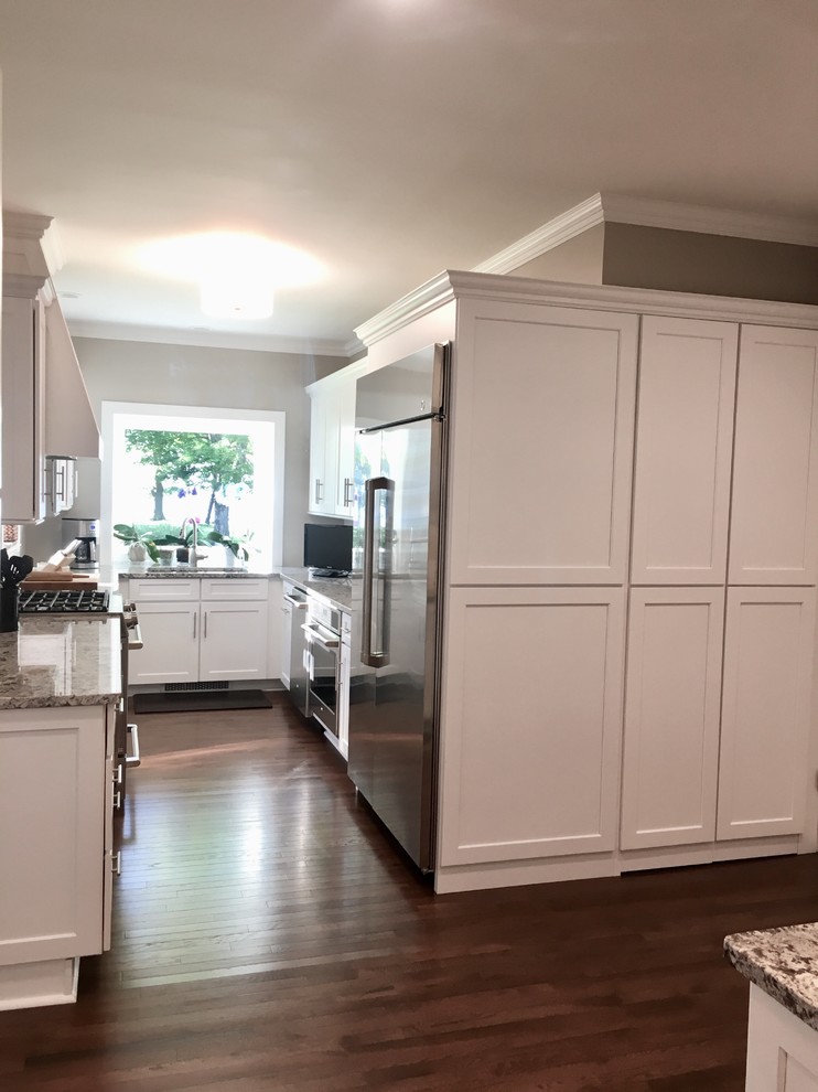 This is an example of a small traditional galley eat-in kitchen in New York with a double-bowl sink, shaker cabinets, white cabinets, solid surface benchtops, white splashback, ceramic splashback, stainless steel appliances, dark hardwood floors, no island, brown floor and multi-coloured benchtop.